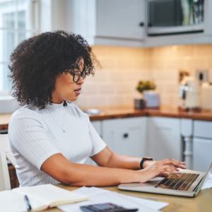 Young women typing on laptop in kitchen paying bills.