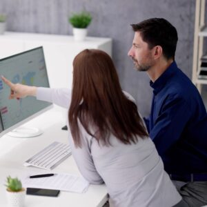 A man and a woman looking at data on two computer monitors.