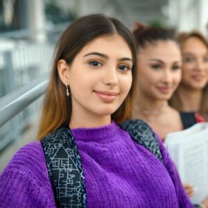 A row of students. The one in the front is wearing a purple sweater and smiling at the camera.