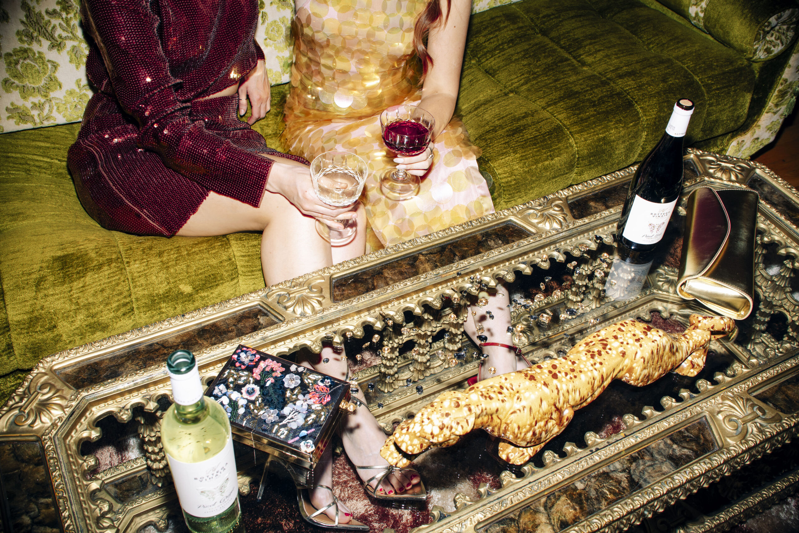 Two women on a couch holding wine with a tray of snacks on a fancy coffee table.